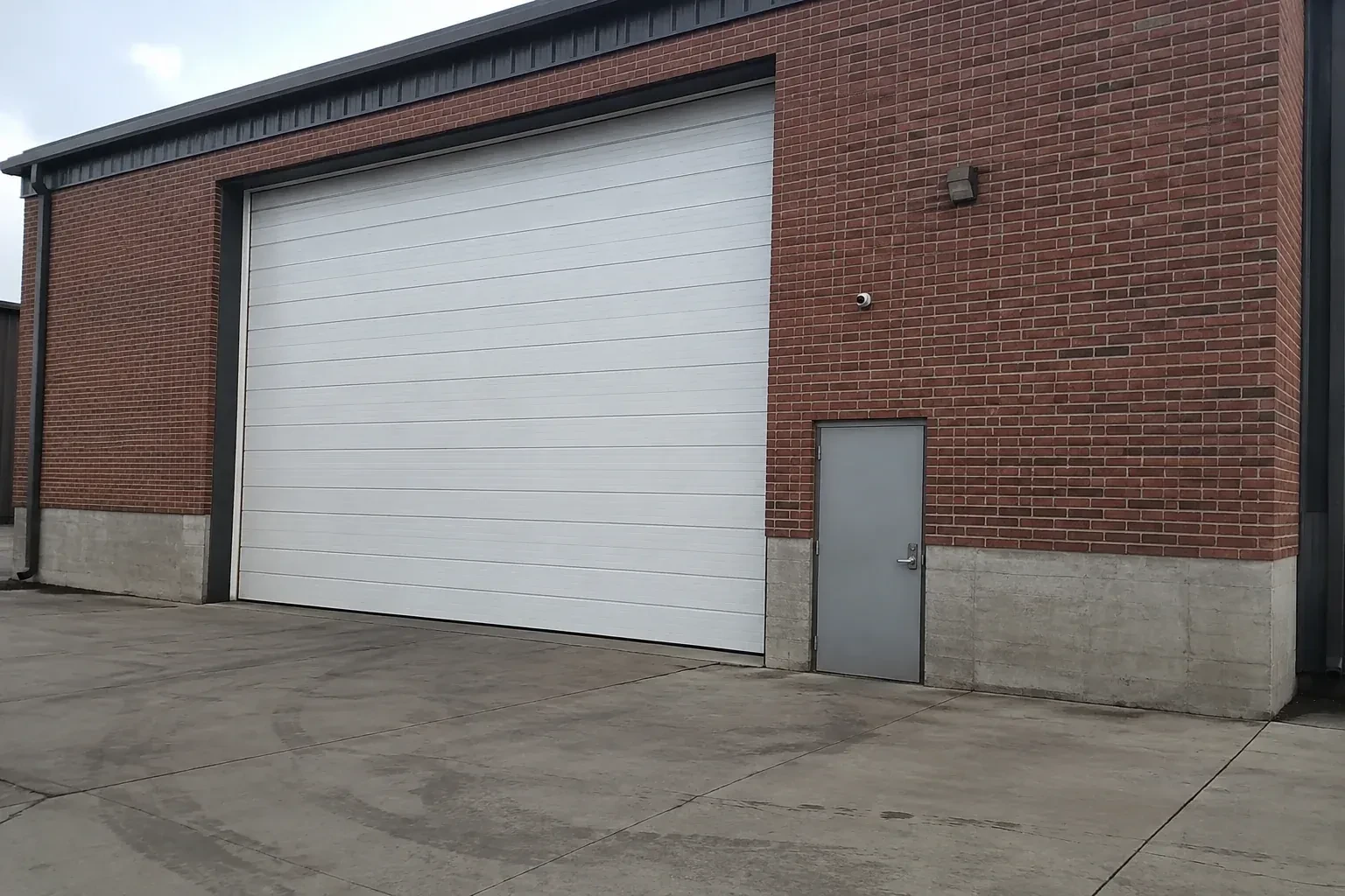 Tall closed sectional loading door beside a personnel door at a brick unit. — Commercial Sectional Door Repair, Owen Sound