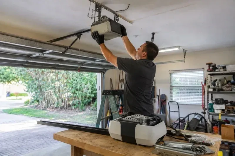 Person holding an overhead garage-door opener beside another opener and hardware on a workbench — Garage Door Opener Replacement, Owen Sound