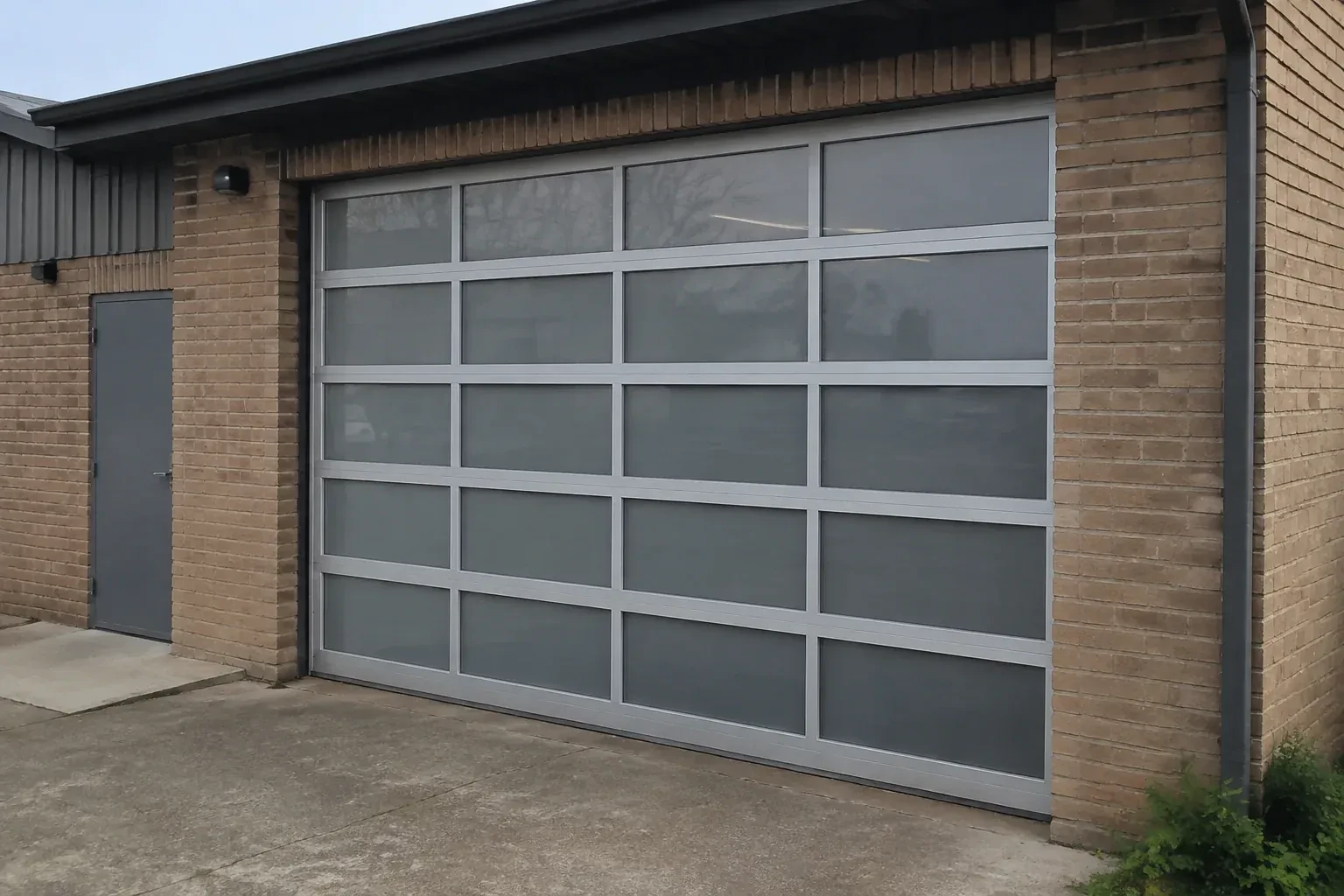 Closed glazed sectional door in a grey metal frame at a brick workshop. — Full-View Glass Garage Door Installation, Owen Sound